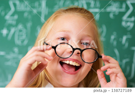 Excited, smile and portrait of child student in classroom with glasses by board for lesson or studying. Education, learning and happy young girl kid with positive attitude for scholarship in school. Excited, smile and portrait of child student in classroom with glasses by board for lesson or studying. Education, learning and happy young girl kid with positive attitude for scholarship in school. 138727189