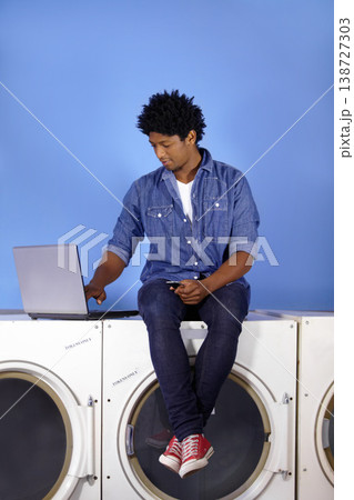 Washing machine, laptop and phone of a black man for laundromat, communication and reading email. Cleaning, typing and a male employee or management of laundry room from the internet with tech Washing machine, laptop and phone of a black man for laundromat, communication and reading email. Cleaning, typing and a male employee or management of laundry room from the internet with tech 138727303