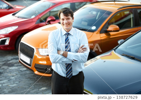 Portrait, smile and a man arms crossed at a dealership for car sale in a commercial parking lot. Business, luxury and automobile trade with a happy young salesman outdoor for transport service 138727629