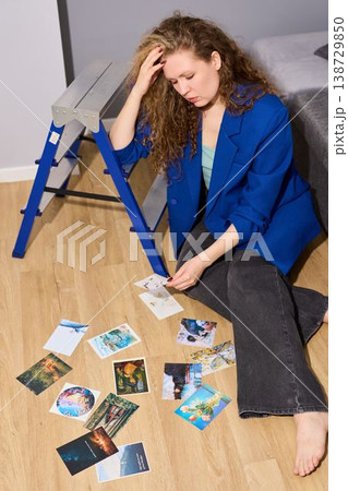 Reflective woman sitting with scattered images and thoughtful gaze Reflective woman sitting with scattered images and thoughtful gaze 138729850