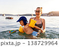 Mother laughing have fun hold child sea swim warm summer sunset. Joyful family vacation candid moment expression playful kid wear armbands splashing water calm seaside coastline travel destination 138729964