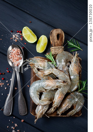 Fresh raw, white-footed shrimp, tiger prawns vannamei, on a wooden cutting board, with lime slices, and seasonings, 138730010