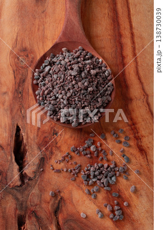 Crystals of black salt, on a wooden spoon, laid out on a wooden surface, top view, 138730039