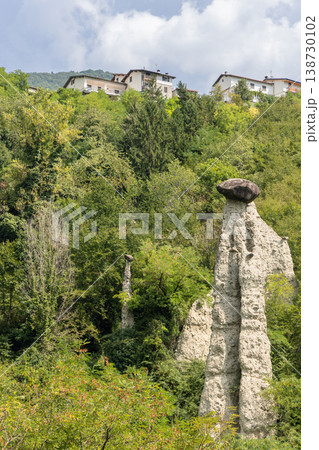 Zone Rock Pyramids in Lombardy with tall white hoodoo capped by dark boulder above green woodland Zone Rock Pyramids in Lombardy with tall white hoodoo capped by dark boulder above green woodland 138730102