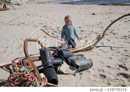 Little 4 year old girl playing with wooden sticks on a sandy beach 138730158