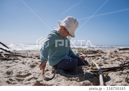 Little 4 year old girl playing with wooden sticks on a sandy beach Little 4 year old girl playing with wooden sticks on a sandy beach 138730165