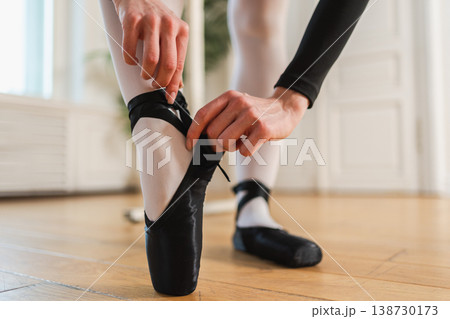 Ballerina puts on pointe shoes on leg in dance class. Classical ballet dancer woman in dance studio. Ballerina putting on tying classical pointe shoes for dance training. Ballet school concept Ballerina puts on pointe shoes on leg in dance class. Classical ballet dancer woman in dance studio. Ballerina putting on tying classical pointe shoes for dance training. Ballet school concept 138730173