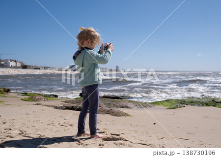Little 4 year old girl taking a photo of the sea with a toy camera on the beach Little 4 year old girl taking a photo of the sea with a toy camera on the beach 138730196