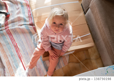 Curious 4 year old girl sitting on a huge delivery box and wondering what is inside 138730198
