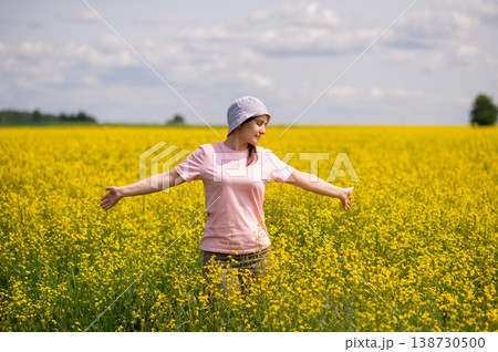Woman in a bucket hat stands in yellow rapeseed field, enjoying the warmth and peace of a sunny summer day Woman in a bucket hat stands in yellow rapeseed field, enjoying the warmth and peace of a sunny summer day 138730500