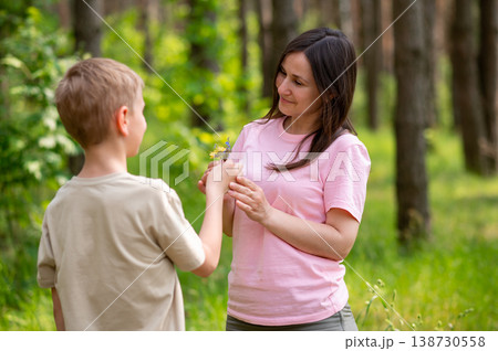 Boy giving a flower to his mother in a sunny forest clearing, tender family moment in nature Boy giving a flower to his mother in a sunny forest clearing, tender family moment in nature 138730558
