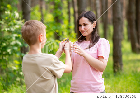 Boy giving a flower to his mother in a sunny forest clearing, tender family moment in nature Boy giving a flower to his mother in a sunny forest clearing, tender family moment in nature 138730559