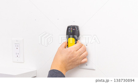 Mans hand pressing yellow stud finder on white wall beside power outlet. Home improvement, final wall scan, DIY confirmation, tool application. Mans hand pressing yellow stud finder on white wall beside power outlet. Home improvement, final wall scan, DIY confirmation, tool application. 138730894