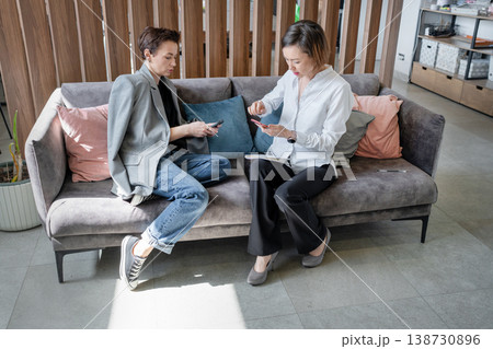 Women in smart clothing sitting on sofa working with laptop and documents in stylish office. Cooperation, teamwork, office, businesswomen, modern. Women in smart clothing sitting on sofa working with laptop and documents in stylish office. Cooperation, teamwork, office, businesswomen, modern. 138730896