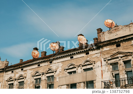 Old residential building with weathered facade and multiple satellite dishes on the roof. Urban decay, outdated infrastructure and contrast between past architecture and modern additions 138732798