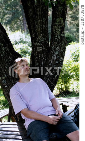 Relaxing man in a park on a bench in summer, enjoying the fresh air, vacation, or relaxing alone in the garden. A thoughtful, smiling, or calm man in nature, resting or waiting in a natural setting. Relaxing man in a park on a bench in summer, enjoying the fresh air, vacation, or relaxing alone in the garden. A thoughtful, smiling, or calm man in nature, resting or waiting in a natural setting. 138733878