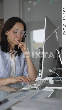 Woman focusing on data entry while typing on a computer, indicating prolonged work, eye strain, and the silent struggle with exhaustion in a professional setting, vertical view Woman focusing on data entry while typing on a computer, indicating prolonged work, eye strain, and the silent struggle with exhaustion in a professional setting, vertical view 138734459
