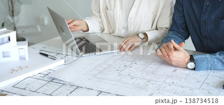 Architects engaging in a professional meeting, reviewing detailed blueprints on a table, utilizing a laptop, and collaborating on building design and construction planning 138734518