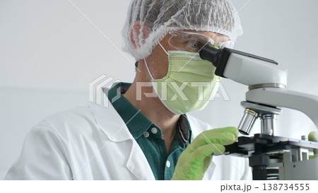 Laboratory scientist analyzing medical sample, wearing green protective gear and conducting research under microscope. Medicine and science concept 138734555