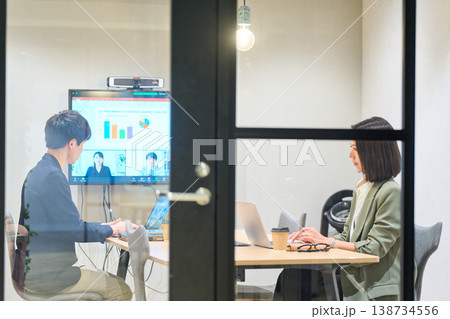 ガラス張りの会議室でリモートチームとWeb会議を行う男女 ガラス張りの会議室でリモートチームとWeb会議を行う男女 138734556