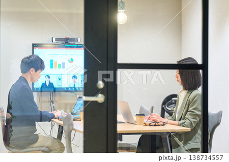 ガラス張りの会議室でリモートチームとWeb会議を行う男女 138734557