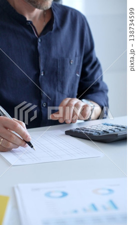 A financial analyst reviewing paperwork, using calculator and laptop while examining corporate budget reports in modern workspace, close up. Audit and taxes, business concept A financial analyst reviewing paperwork, using calculator and laptop while examining corporate budget reports in modern workspace, close up. Audit and taxes, business concept 138734599