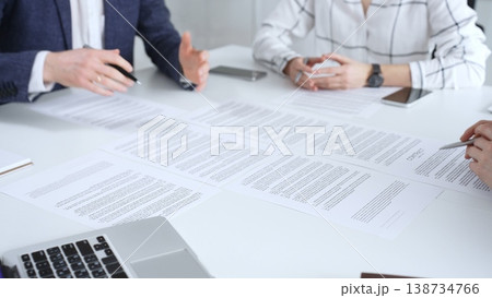 Professionals reviewing and signing contract documents across a white table, hands exchanging papers and pens to finalize negotiation, partnership and corporate agreement decisions 138734766