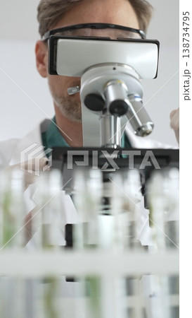 Scientific researcher in protective gear analyzing specimens through a microscope in a sterile laboratory environment. Medicine, healthcare and science concept Scientific researcher in protective gear analyzing specimens through a microscope in a sterile laboratory environment. Medicine, healthcare and science concept 138734795