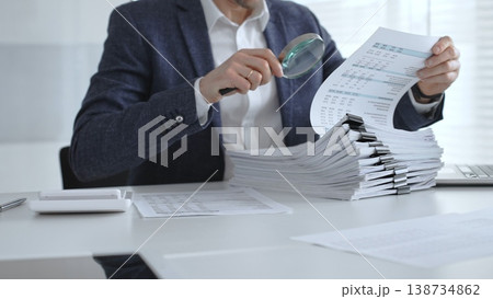 Professional reviewing corporate financial statements with magnifying glass, auditing reports, taxes and expense details. Audit and taxes Professional reviewing corporate financial statements with magnifying glass, auditing reports, taxes and expense details. Audit and taxes 138734862