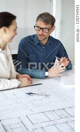 Architects collaborating on blueprint plans, discussing engineering details and project designs, planning construction development with a laptop in a modern office environment 138734941