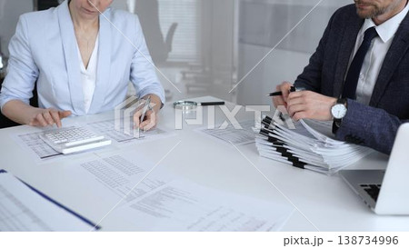 Business professionals collaborating at a desk, using a calculator and organizing financial documents for accounting, tax preparation, budgeting and corporate finance management. Audit and taxes Business professionals collaborating at a desk, using a calculator and organizing financial documents for accounting, tax preparation, budgeting and corporate finance management. Audit and taxes 138734996