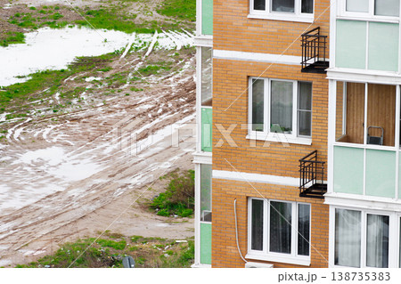 Red brick facade of high apartment building in closeup, surrounding muddy ground and rainwater. Windows and balconies, rain or poor weather. Typical residential location Red brick facade of high apartment building in closeup, surrounding muddy ground and rainwater. Windows and balconies, rain or poor weather. Typical residential location 138735383