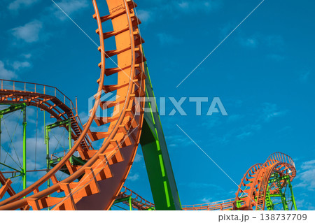 Abstract detail of empty orange roller coaster loops against a bright blue sky Abstract detail of empty orange roller coaster loops against a bright blue sky 138737709