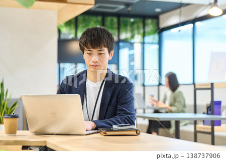 企業のオープンオフィスでノートパソコンを使い作業する若い男性 企業のオープンオフィスでノートパソコンを使い作業する若い男性 138737906