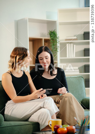 Two women collaborating on a project at home, brainstorming with a laptop and notebook in a cozy setting. Two women collaborating on a project at home, brainstorming with a laptop and notebook in a cozy setting. 138739396