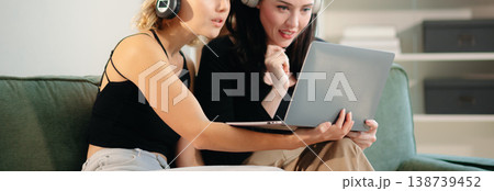Two women collaborating on a project at home, brainstorming with a laptop and notebook in a cozy setting. Two women collaborating on a project at home, brainstorming with a laptop and notebook in a cozy setting. 138739452