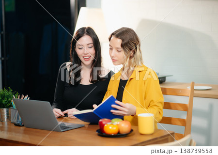 Two professional women collaborating on a business project with a laptop, notebook, and coffee at home. Two professional women collaborating on a business project with a laptop, notebook, and coffee at home. 138739558