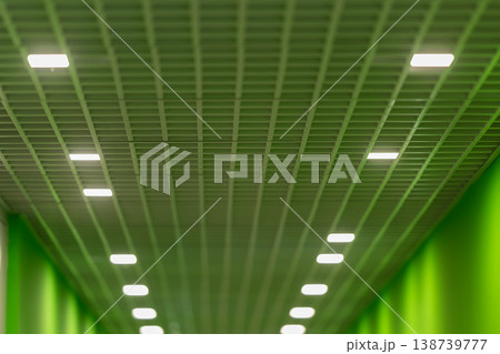 Green tones with illuminated ceiling. Urban corridor featuring illuminated grid and acoustic panels. Nighttime city passage illuminated by geometric lights and cool hues Green tones with illuminated ceiling. Urban corridor featuring illuminated grid and acoustic panels. Nighttime city passage illuminated by geometric lights and cool hues 138739777