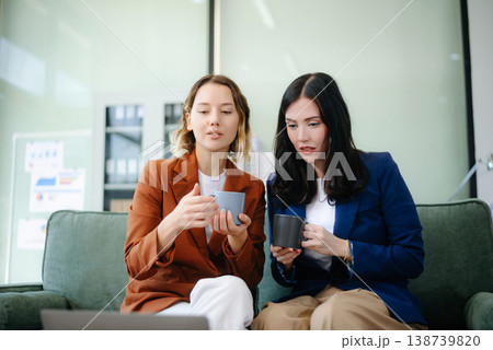 Two women collaborating on a project on sofa at home, brainstorming with a laptop and notebook Two women collaborating on a project on sofa at home, brainstorming with a laptop and notebook 138739820