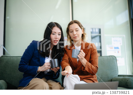 Two women collaborating on a project on sofa at home, brainstorming with a laptop and notebook 138739821