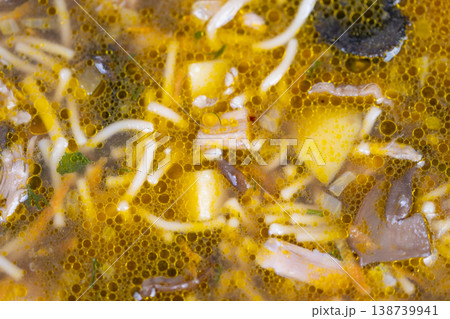 Closeup homemade mushroom soup glistening with golden oil droplets, soft noodles, mushroom pieces and diced root vegetable, mealprep friendly comfort ready for storage 138739941