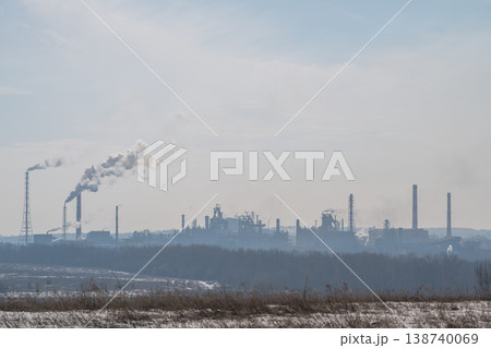 Metallurgical plant on distant horizon at dawn, soft early light and rising vapor, cooling towers and cranes creating silhouettes, snowy foreground and tranquil industrial mood 138740069