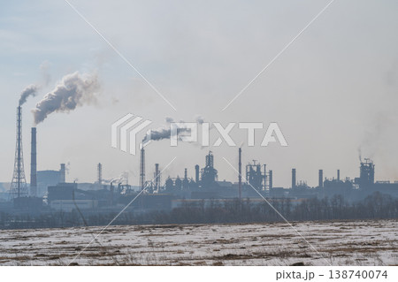 Factories belching smoke over fields. Lazy clouds fade behind distant refinery structures. Muted gray sky over desolate industrial landscape signifies environmental worries 138740074