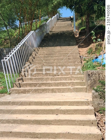 Concrete Outdoor Stairs With White Railing Rising Uphill Through Green Trees and Sunlit Pathway 138740086