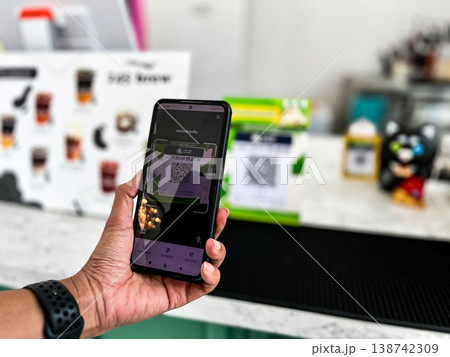 a person using a smartphone to scan a QR code for digital payment at a cafe counter. Modern cashless transaction, mobile banking, and contactless technology in everyday lifestyle a person using a smartphone to scan a QR code for digital payment at a cafe counter. Modern cashless transaction, mobile banking, and contactless technology in everyday lifestyle 138742309