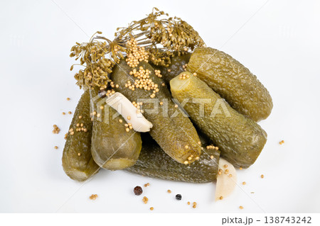 Pickled cucumbers heaped with aromatic dill and scattered seeds on white surface, glossy brine sheen and firm texture convey market fresh preserved produce and small batch appeal 138743242