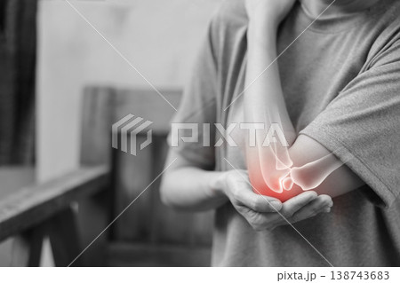 Monochrome photo of woman suffering from severe elbow pain, holding her arm with a red glowing anatomical bone graphic overlay showing joint inflammation, arthritis, or injury in medical concept. Monochrome photo of woman suffering from severe elbow pain, holding her arm with a red glowing anatomical bone graphic overlay showing joint inflammation, arthritis, or injury in medical concept. 138743683