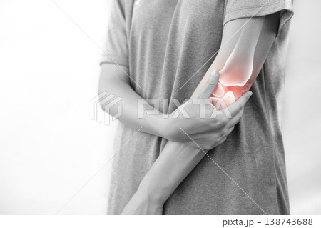 Monochrome photo of woman suffering from severe elbow pain, holding her arm with a red glowing anatomical bone graphic overlay showing joint inflammation, arthritis, or injury in medical concept. 138743688