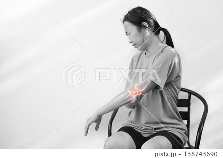 Monochrome photo of woman suffering from severe elbow pain, holding her arm with a red glowing anatomical bone graphic overlay showing joint inflammation, arthritis, or injury in medical concept. 138743690