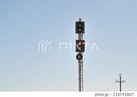 Red signal alert. Vivid warning sign amidst tranquil sky and distant poles. Bright crimson signal standing guard under muted sky with distant poles and subtle lights 138743807